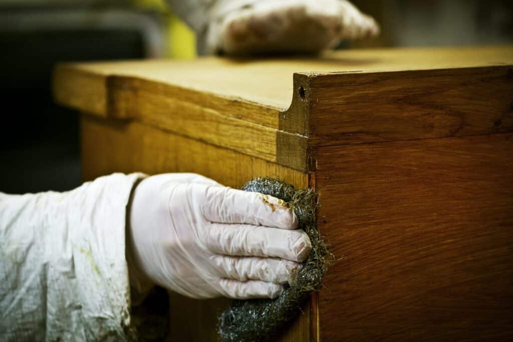 A person in gloves using wire wool to sand down or wax a piece of furniture.
