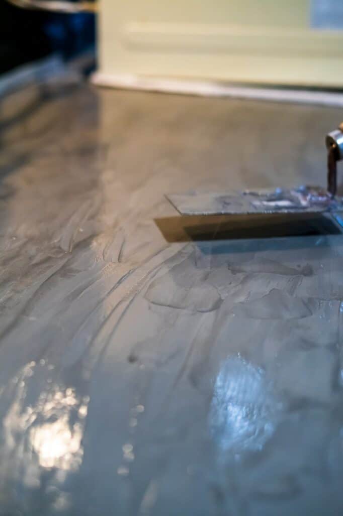 closeup of concrete plaster coating on the kitchen table top with a trowel in the background.