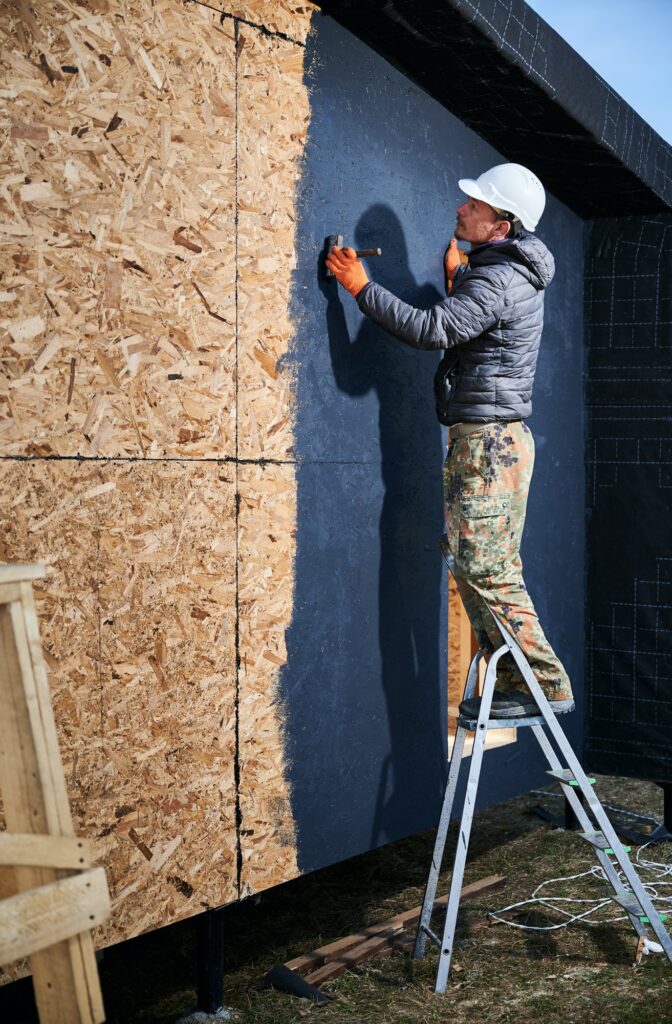 Male painter using paint roller, doing exterior paint work while building wooden frame house.