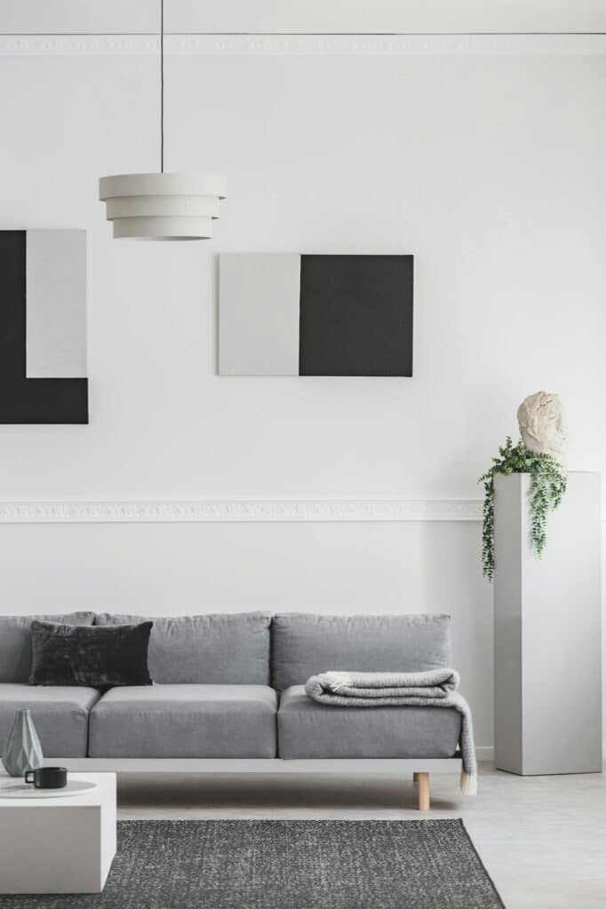 Fabre Occitanie - Un salon moderne avec un canapé gris, un tapis géométrique, une suspension blanche, des œuvres murales abstraites en noir et blanc inspirées de Fabre Occitanie et une sculpture sur socle.