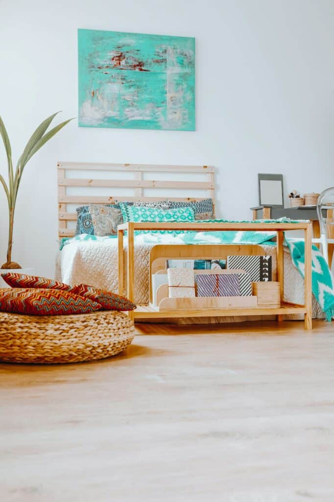 Fabre Occitanie - Une chambre cosy de style bohème avec un lit bas en bois, des oreillers colorés, un petit bureau et une plante, le tout sous une œuvre d'art bleu serein de Fabre Occitanie.