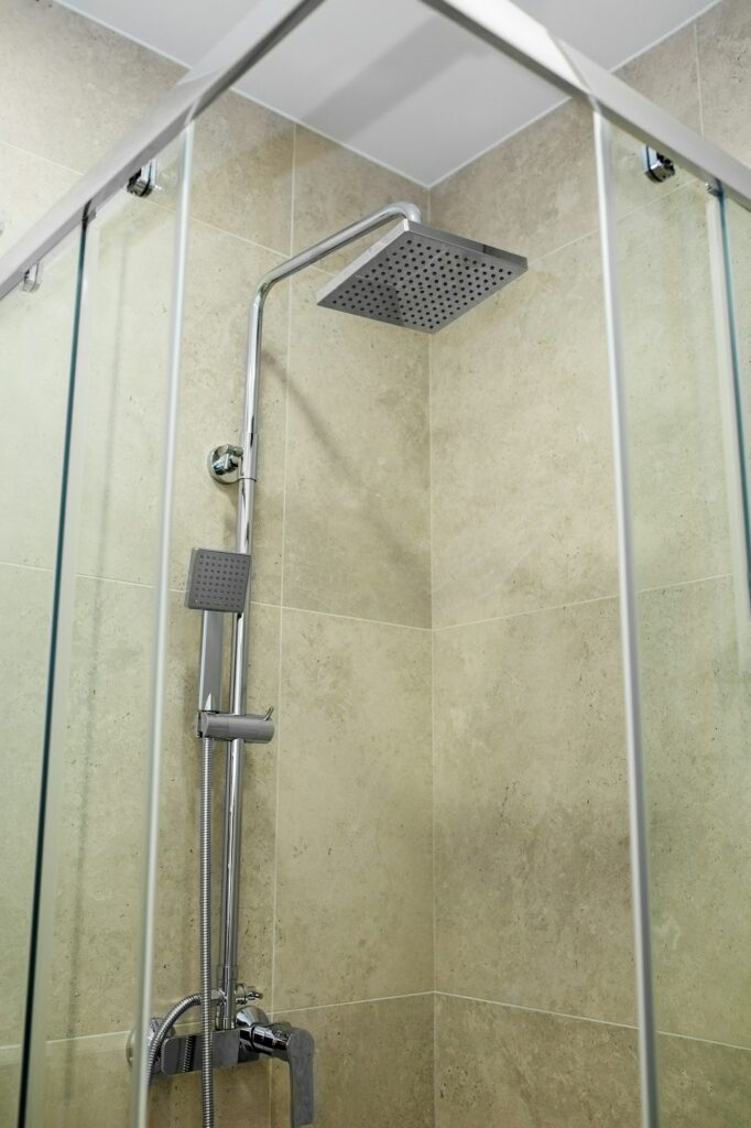 Fabre Occitanie - Cabine de douche moderne avec portes vitrées, pomme de douche murale Fabre Occitanie et douchette réglable dans une salle de bain carrelée.