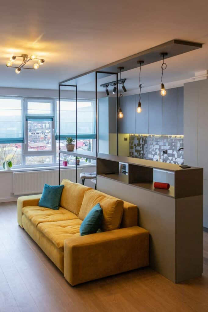 Fabre Occitanie - Salon moderne avec canapé moutarde, coussins décoratifs et vue sur la cuisine dans un appartement.