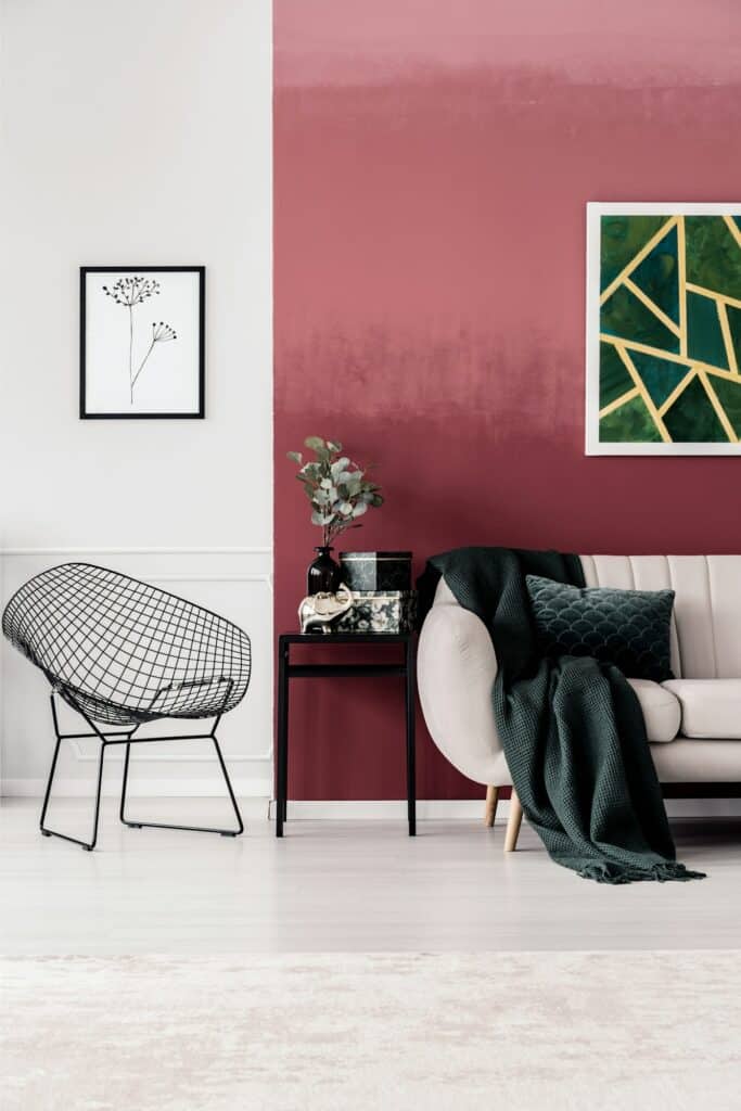 Fabre Occitanie - Salon moderne avec un mur bicolore rose et blanc, comprenant une élégante chaise en fil noir, un canapé blanc avec un jeté vert et une table d'appoint avec une plante et Fabre Occitanie