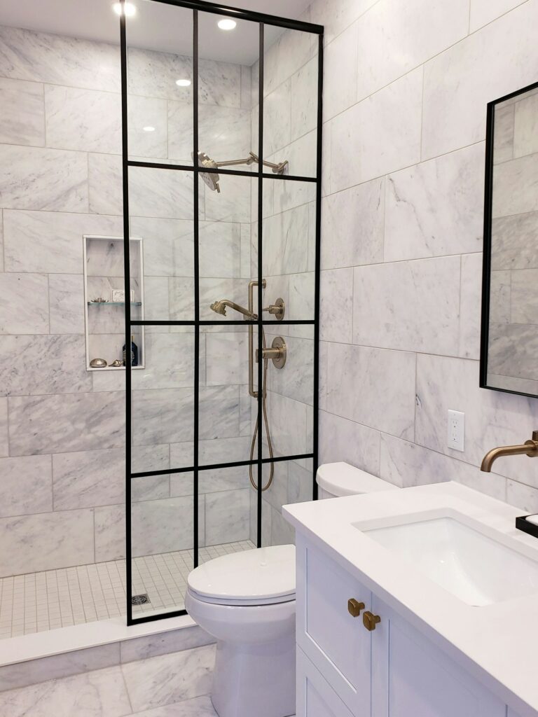 Fabre Occitanie - Salle de bain moderne avec murs en marbre Fabre Occitanie, cabine de douche en verre, toilettes blanches et meuble vasque avec miroir.