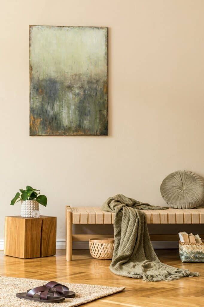 Fabre Occitanie - Un coin chambre cosy avec banquette en bois, plaid gris, tableau Fabre Occitanie au mur et plantes décoratives à proximité.