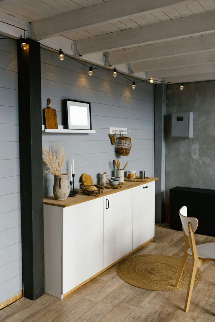 Fabre Occitanie - Un coin cuisine moderne avec une armoire blanche, des comptoirs en bois et un éclairage décoratif suspendu au-dessus. Un tapis rond en jute et une chaise en bois sont positionnés sur le sol en béton Fabre Occitanie.