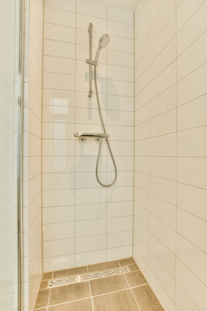 Fabre Occitanie - Coin salle de bain moderne et épuré avec porte de douche en verre et douche carrelée beige Fabre Occitanie avec pomme de douche à main en acier inoxydable.