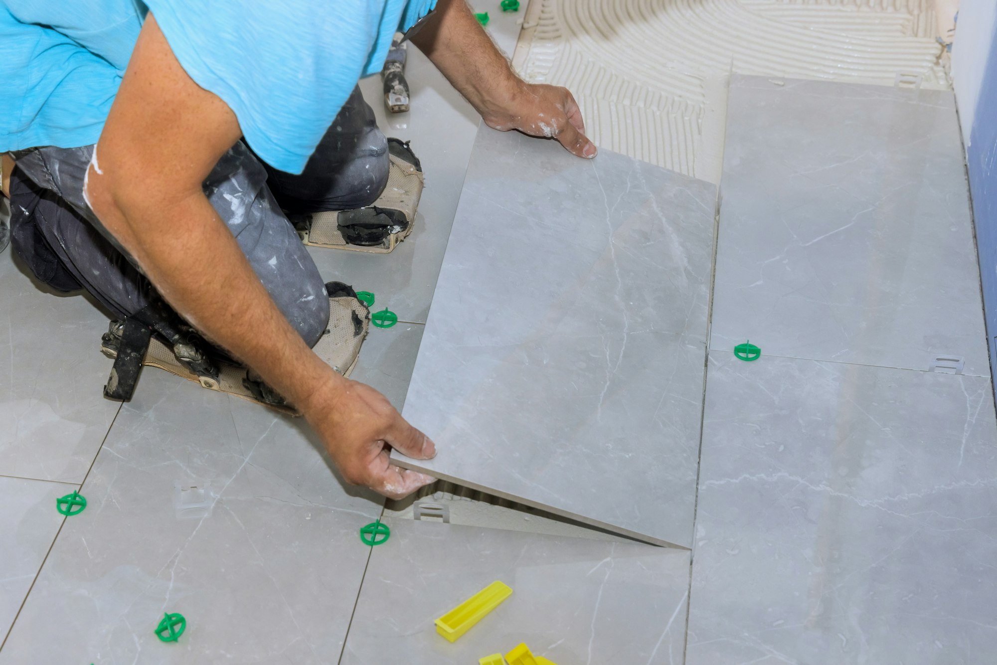 Tiler worker lay large tiles on ceramic floor tile over a mortar adhesive