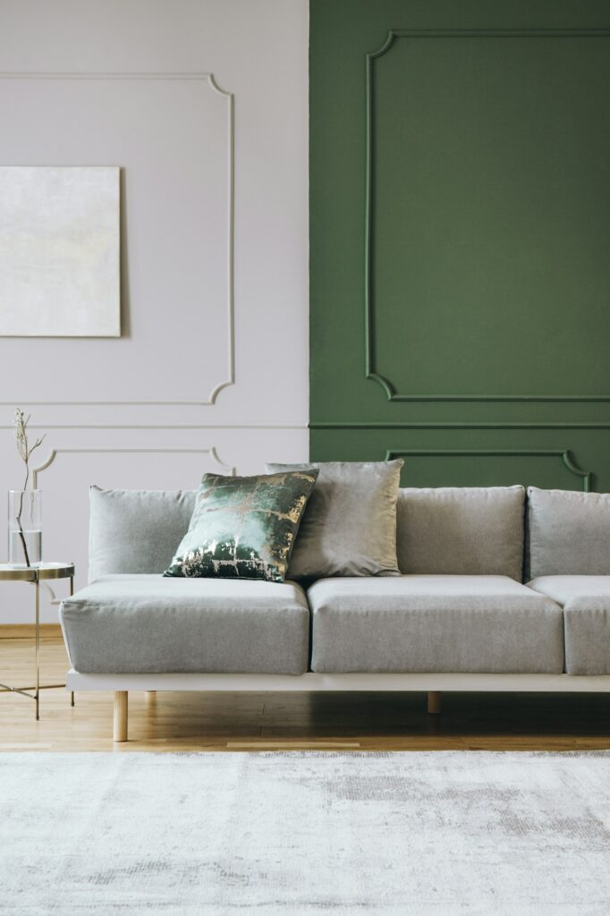 Fabre Occitanie - Salon moderne avec un canapé gris clair, un mur d'accent vert influencé par les tons Fabre Occitanie et des œuvres d'art murales abstraites. La décoration comprend des tons terreux subtils et un design minimaliste.