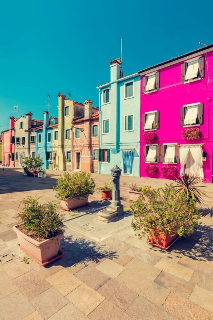 Fabre Occitanie - Des bâtiments colorés dans des tons vibrants de rose, de bleu et de jaune bordent une place de Fabre Occitanie, sous un ciel bleu clair.