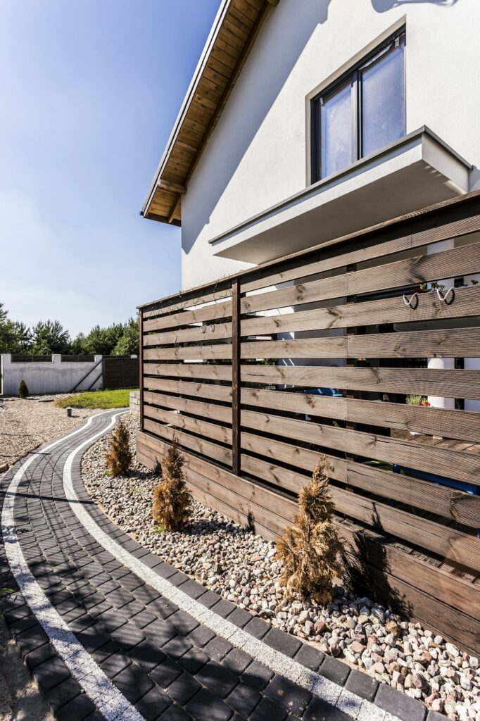 Fabre Occitanie - Maison d'habitation moderne à Fabre, Occitanie, avec une clôture en bois et une allée pavée bordée de petits buissons et de pierres sous un ciel bleu clair.