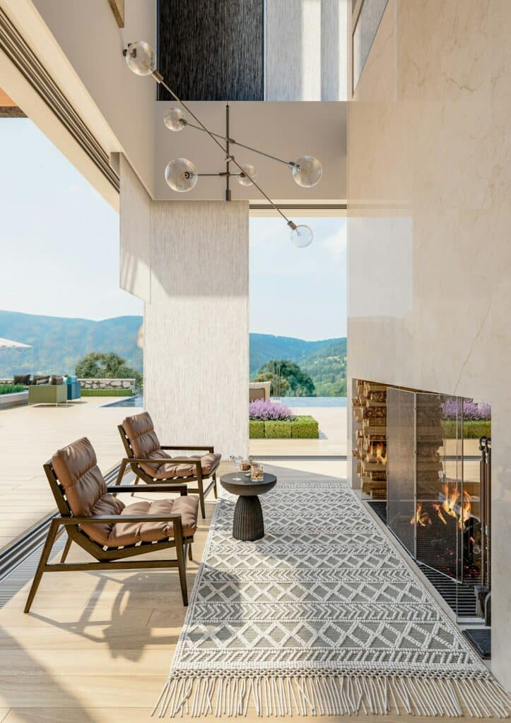 Fabre Occitanie - Patio moderne avec deux chaises en cuir, un tapis géométrique et une cheminée allumée donnant sur la vue panoramique sur les montagnes de Fabre Occitanie.