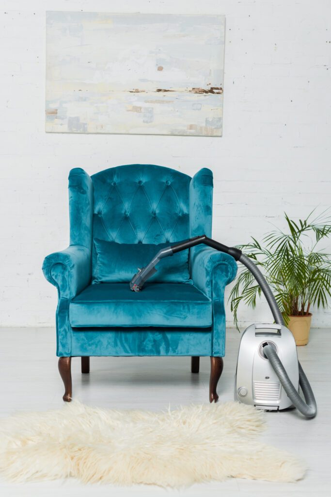 Fabre Occitanie - Un fauteuil rembourré bleu sarcelle avec un tuyau d'aspirateur métallique sur son bras, posé contre un mur blanc avec des œuvres d'art et une plante en pot à Fabre Occitanie.